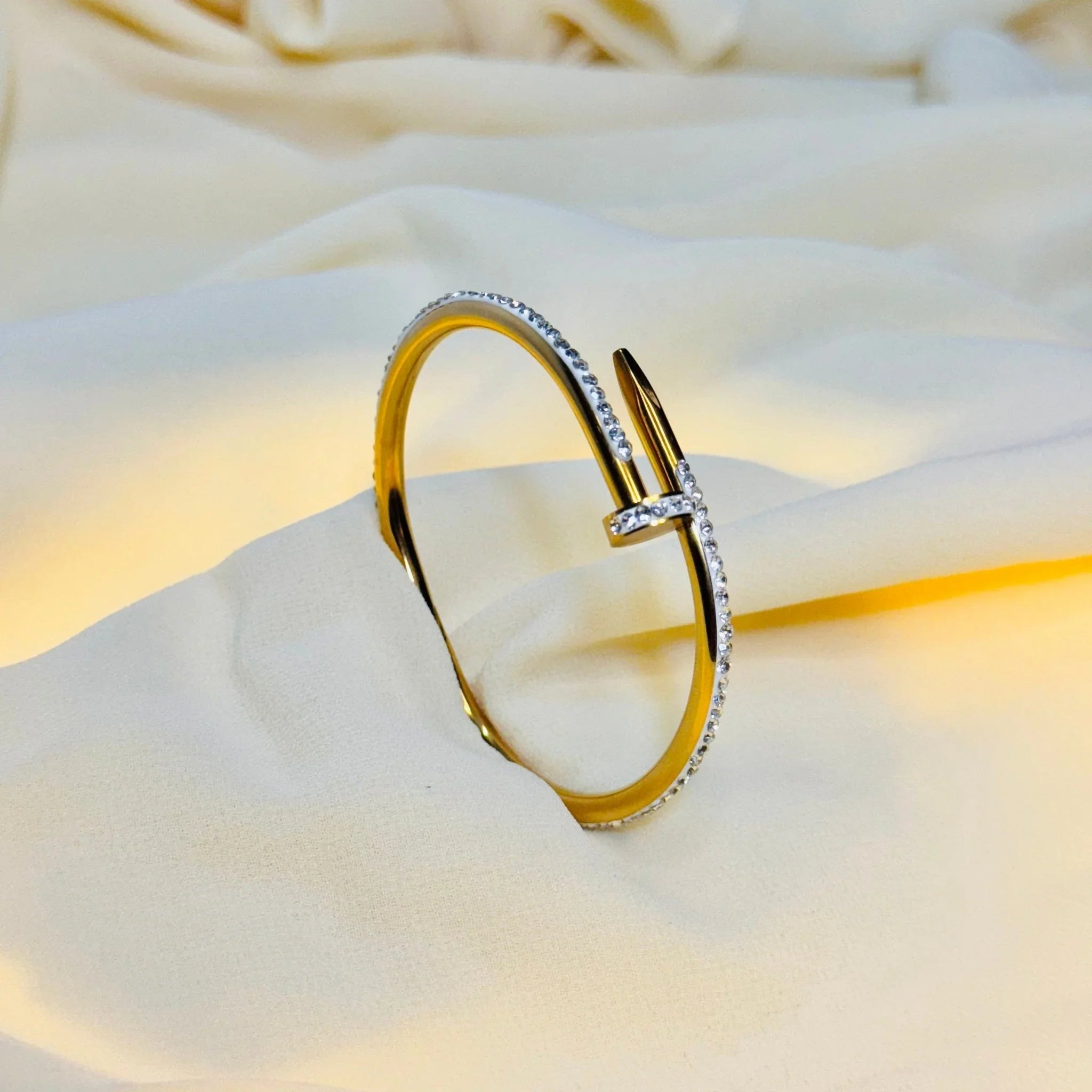 Gold bracelet with embedded white crystals placed on soft beige fabric background