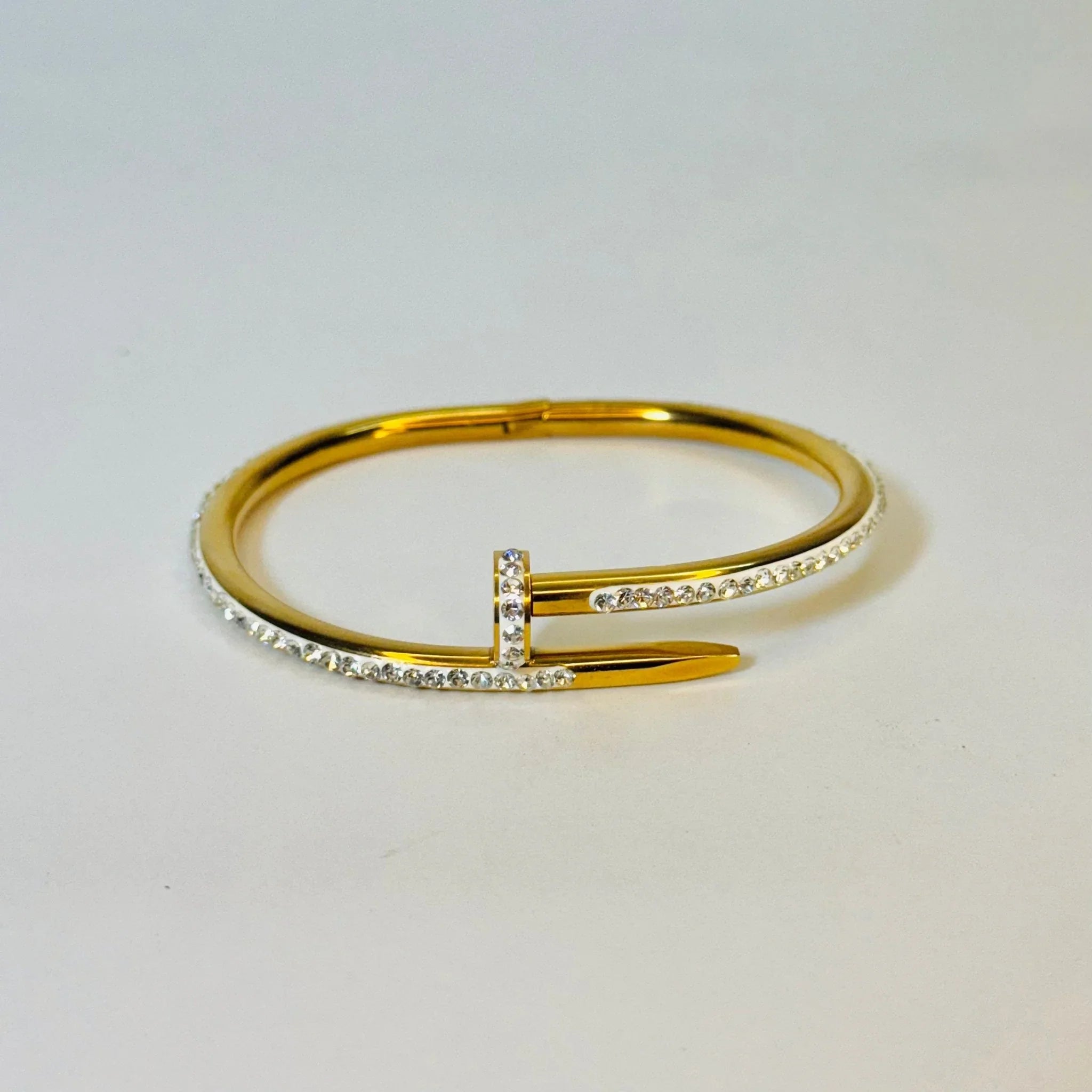 Gold bangle bracelet designed like a nail, adorned with small clear crystals on a white background