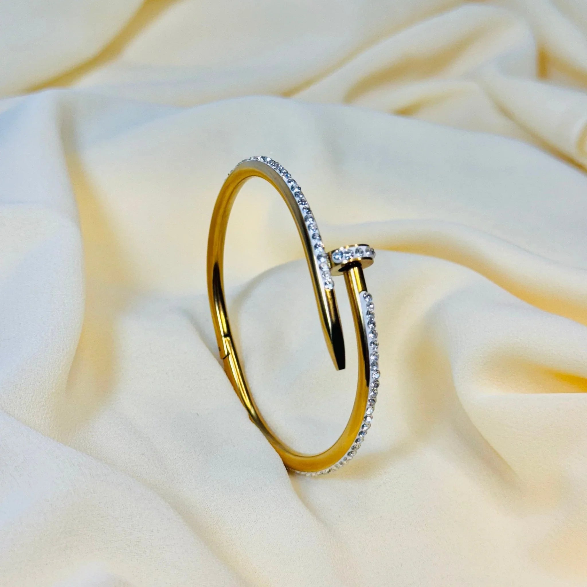 Gold bangle bracelet with embedded clear crystals on soft cream fabric background