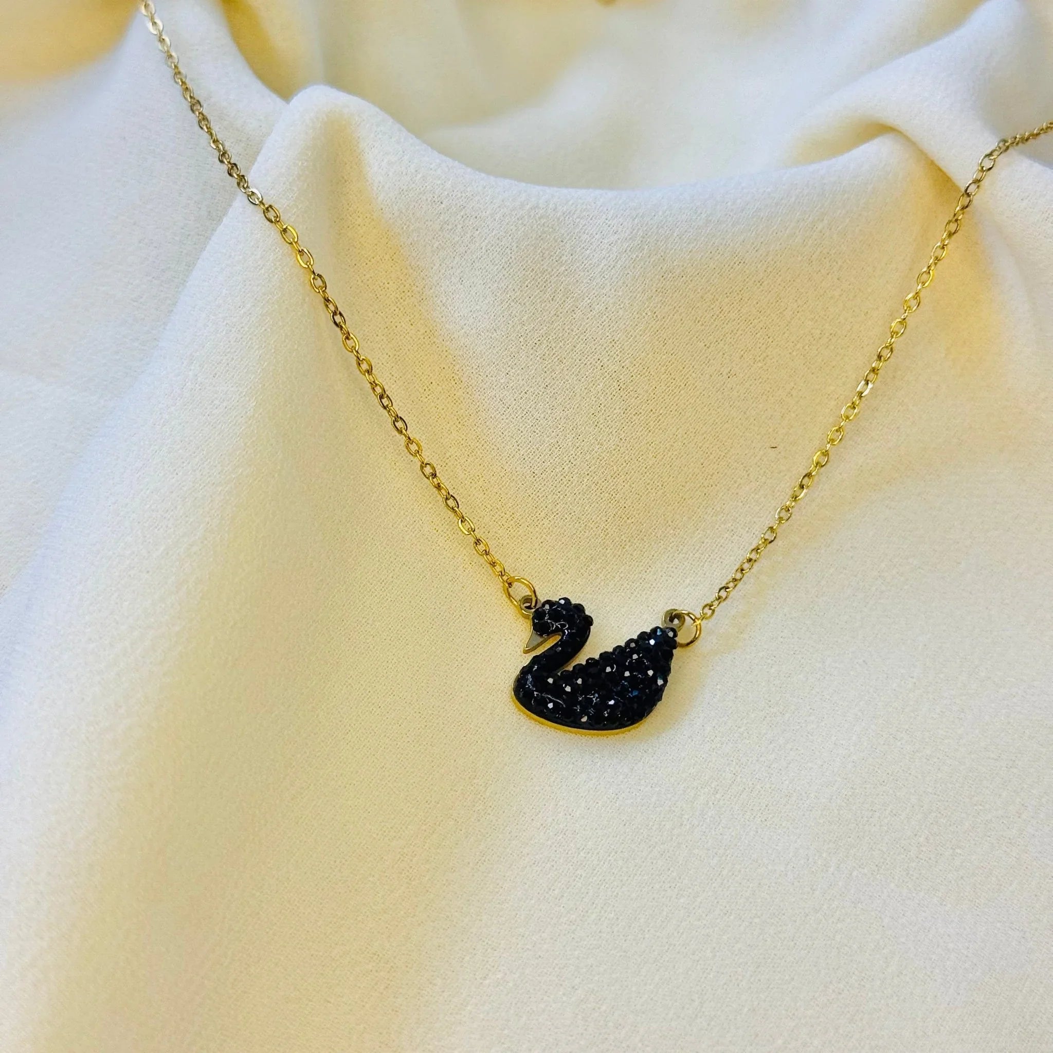 Gold chain necklace with a black swan pendant encrusted with black crystals on white fabric