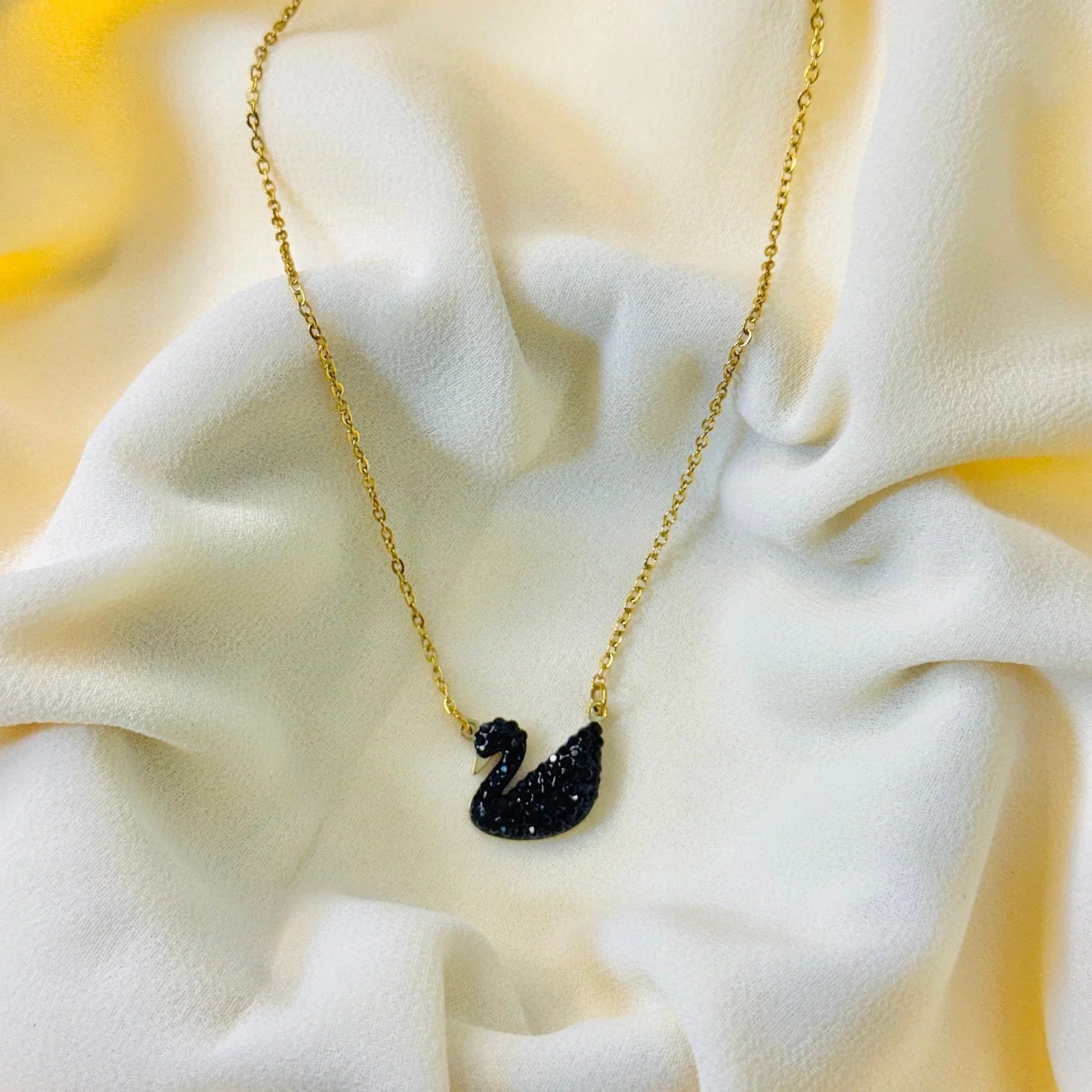 Gold chain necklace with black swan pendant on soft white fabric background