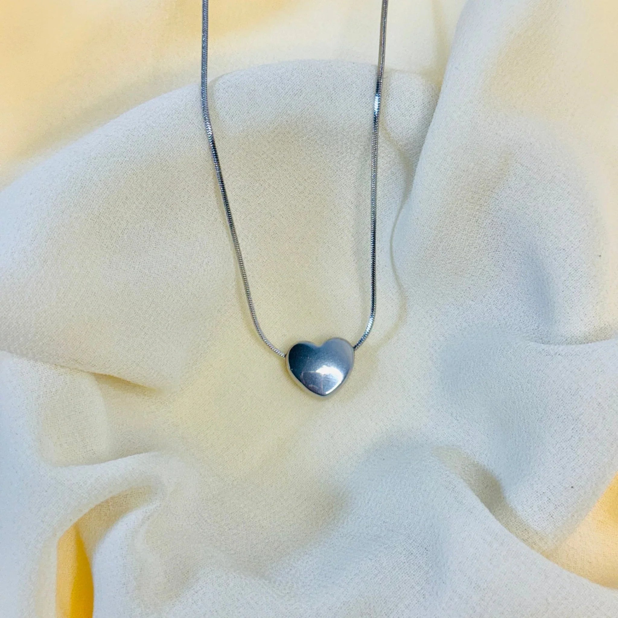 Silver heart pendant necklace on soft textured white fabric background