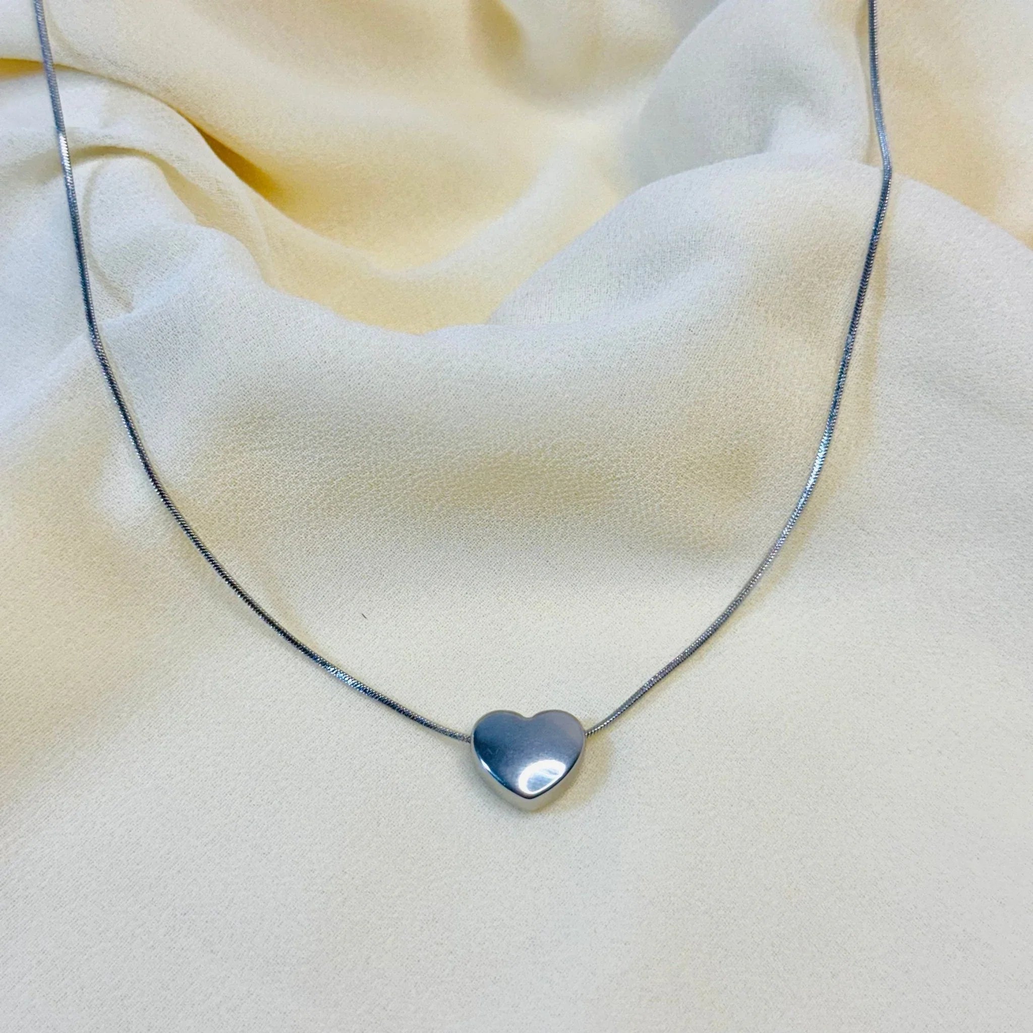 Silver heart pendant necklace on soft beige fabric background