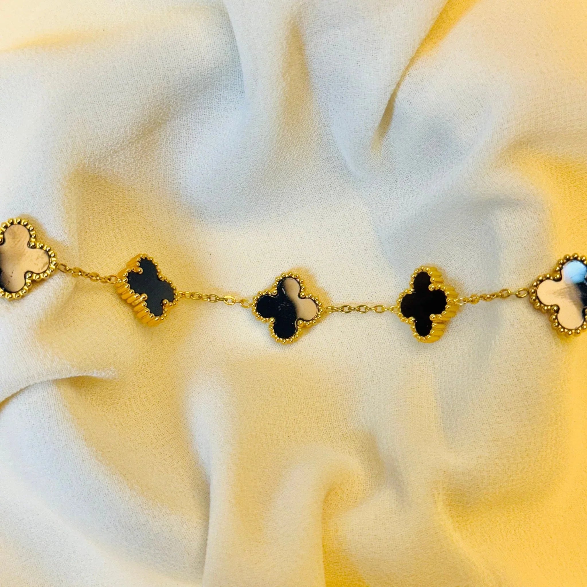 Gold bracelet with black and white clover-shaped charms on soft cream fabric